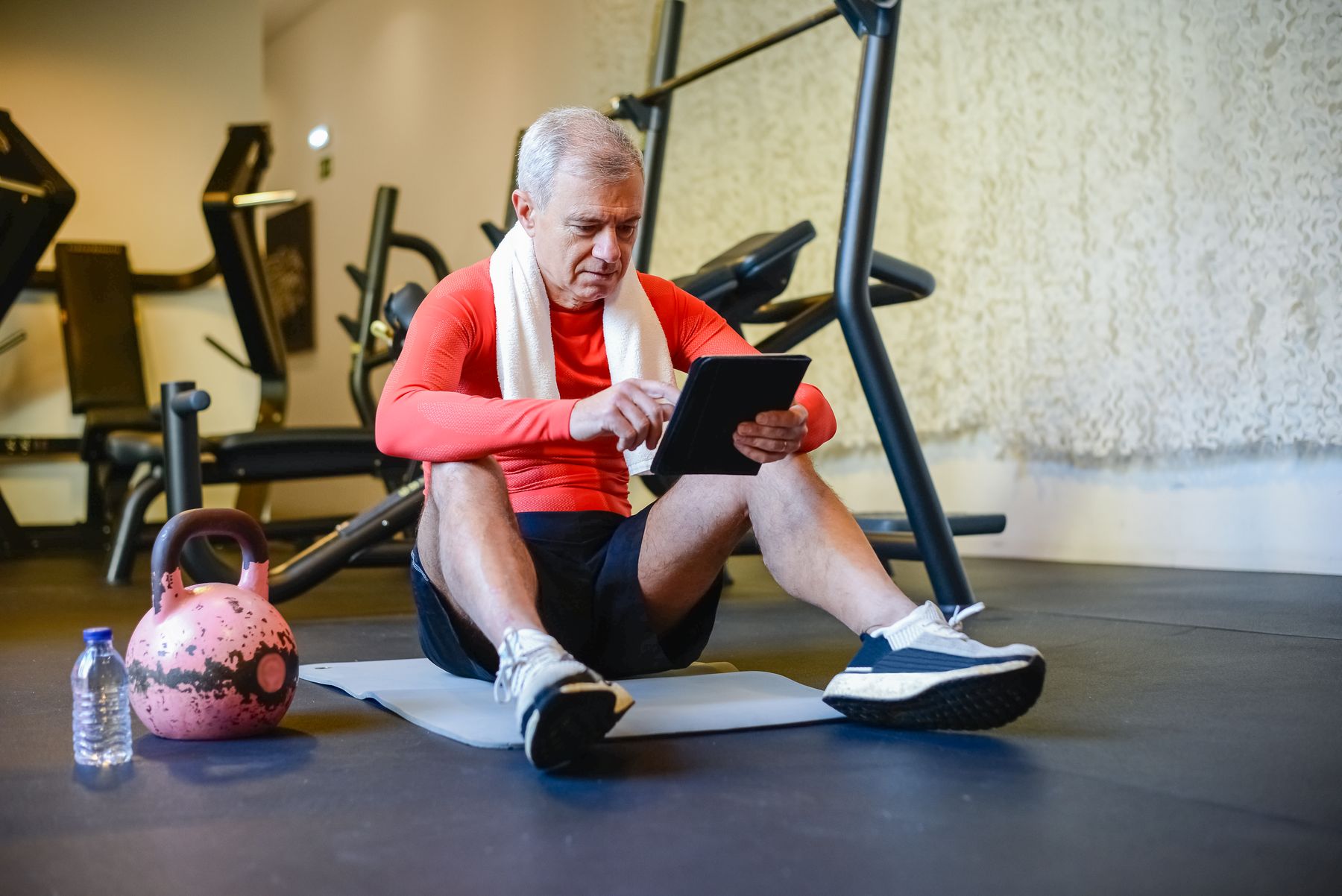 A gym member uses a tablet to review workout guidance between exercises.