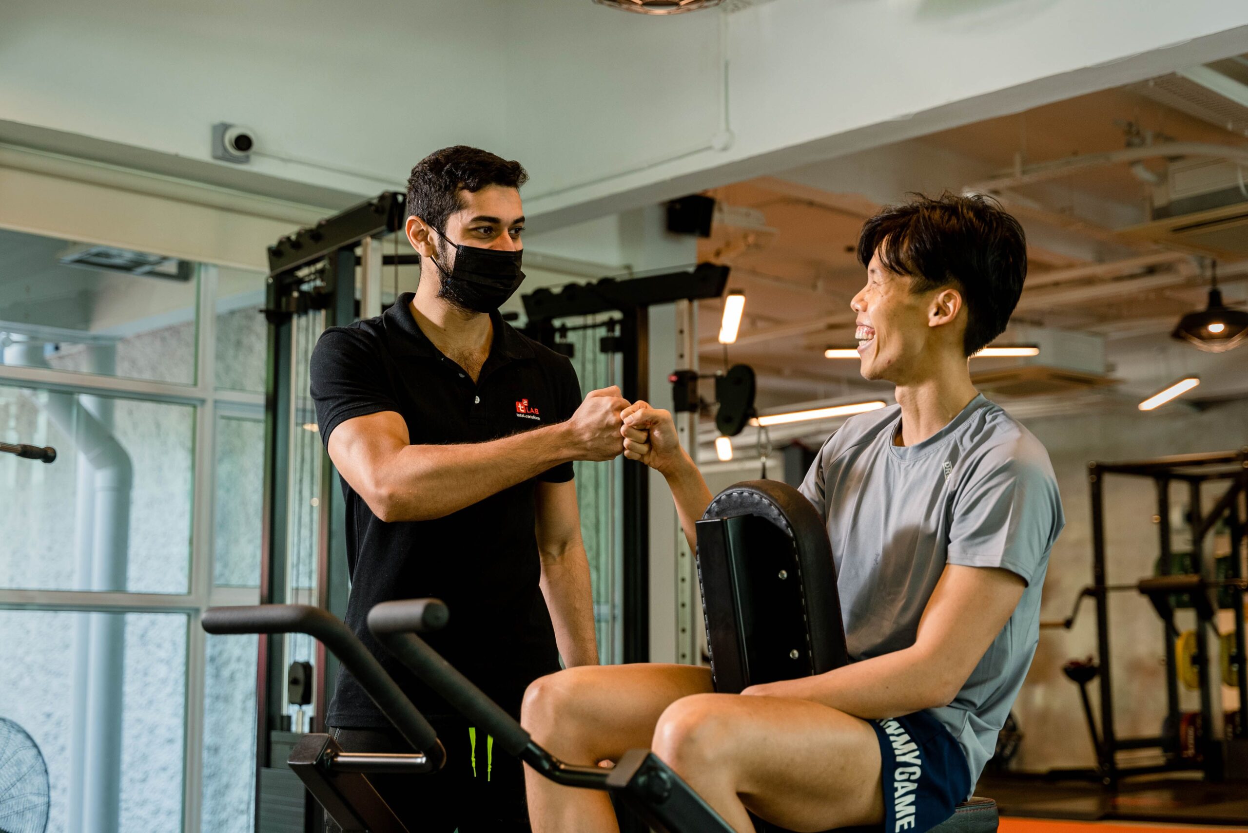 A personal trainer and gym member celebrate progress with a fist bump after a training session.